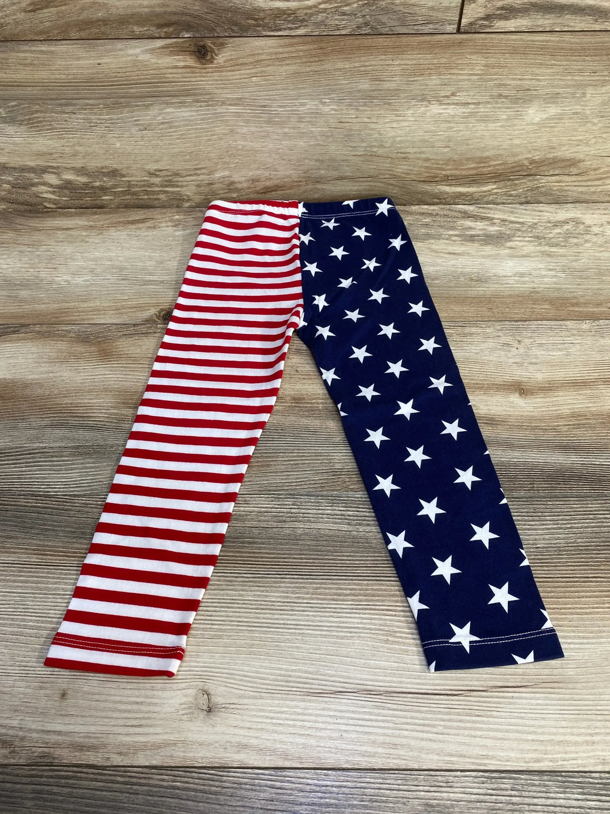 Flat lay of toddler leggings showing red-and-white striped left leg and navy right leg with white stars, elastic waist on light wood background