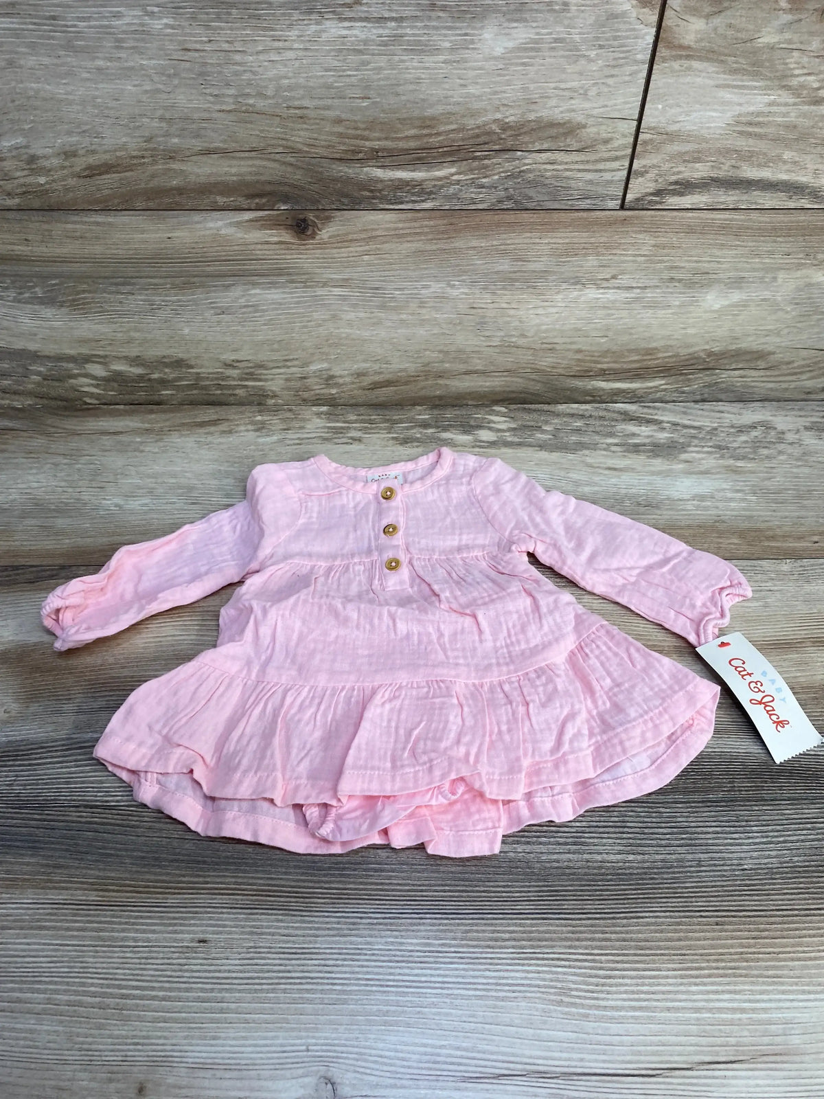 Front view of Cat and Jack pink muslin henley dress with bloomers, long sleeves and wooden buttons, laid flat on wood background
