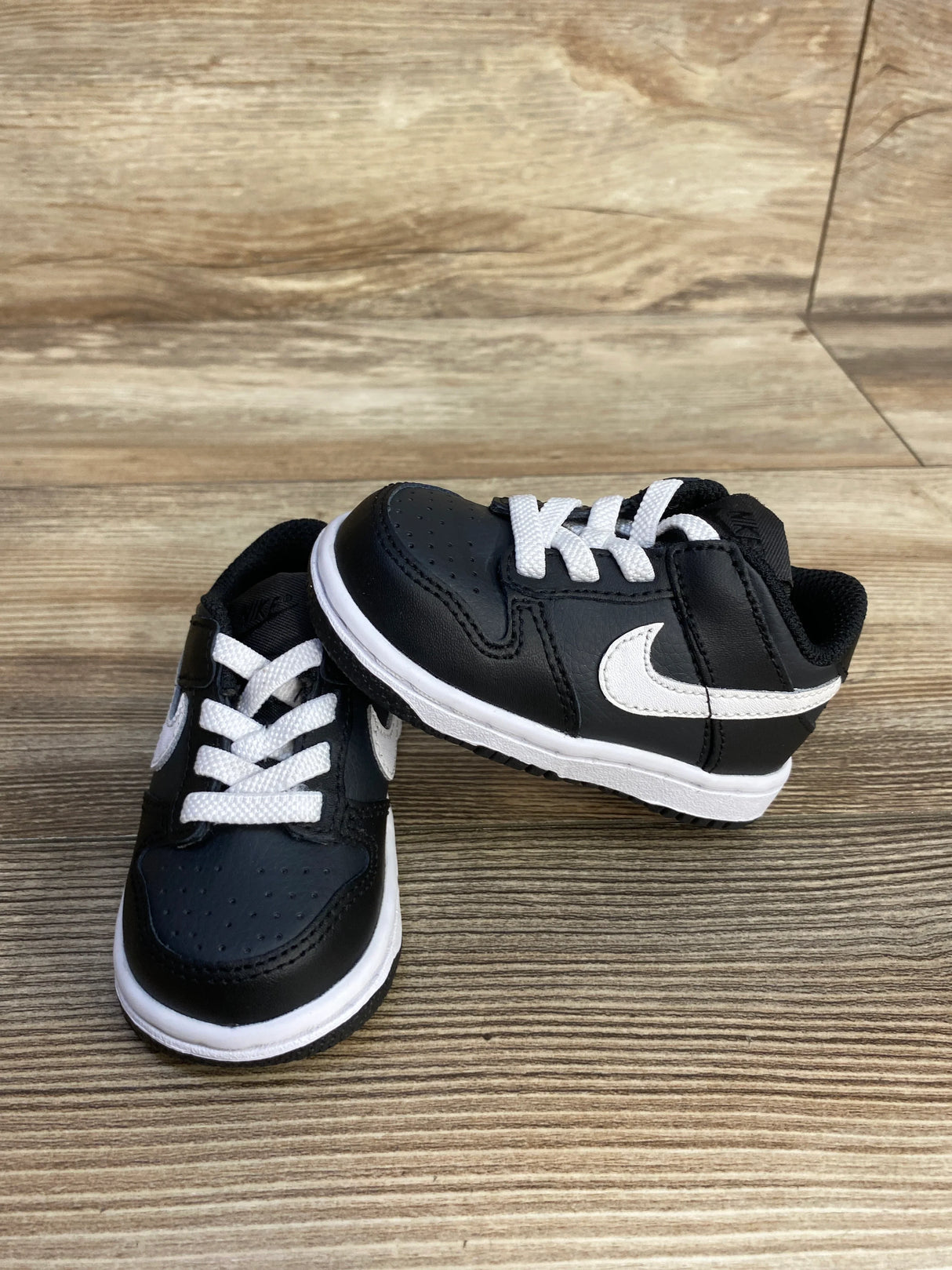 Black baby Nike sneakers with white swoosh and laces on wood background