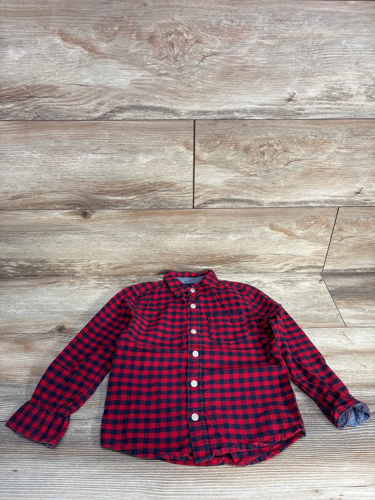 Red and black checkered long-sleeve button-up shirt laid flat on wood floor