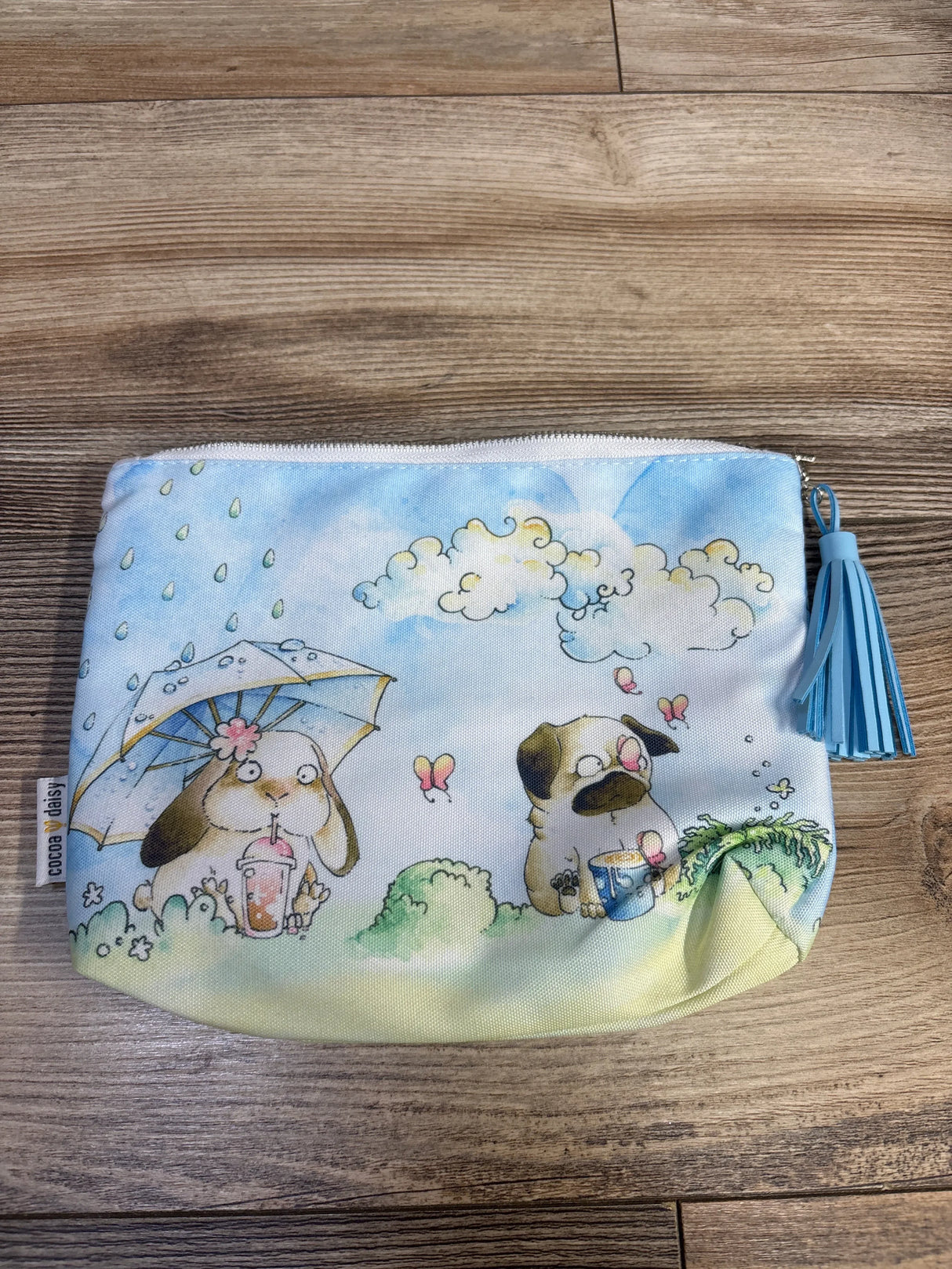 Cocoa Daisy pouch with cute dog illustrations, blue tassel zipper, on wood background