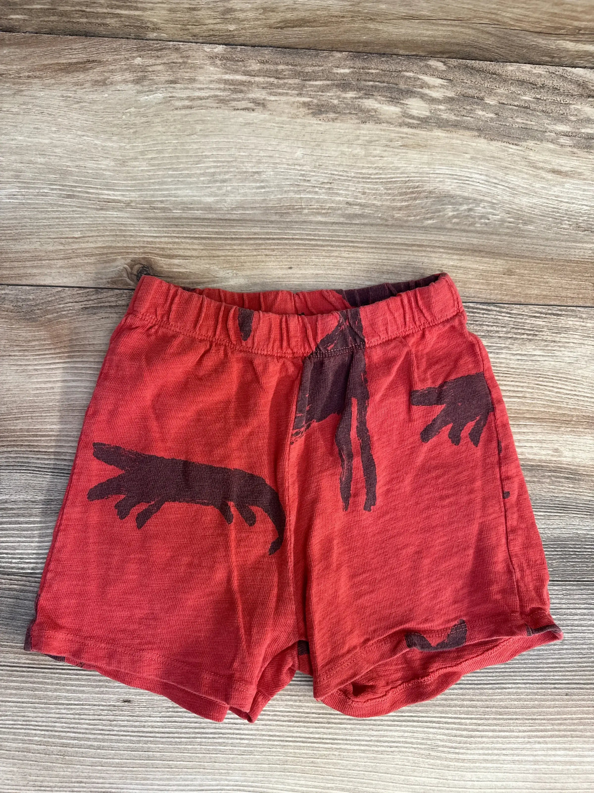 Flat lay of red Zara toddler shorts showcasing dark brown fox print and elastic waistband on wood background