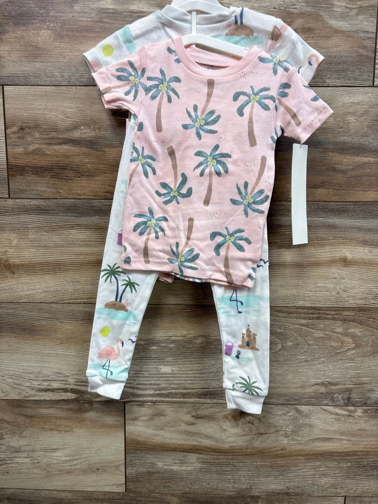 Front view of toddler pajama set size 2T, pink palm tree tee and white flamingo print leggings on hanger against wood floor
