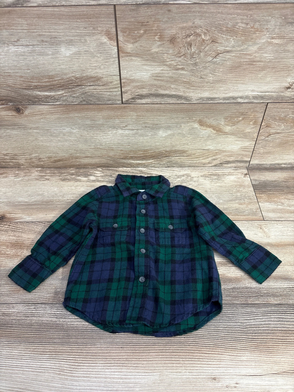 Toddler's green and navy blue plaid button-up flannel shirt laid on wooden floor backdrop