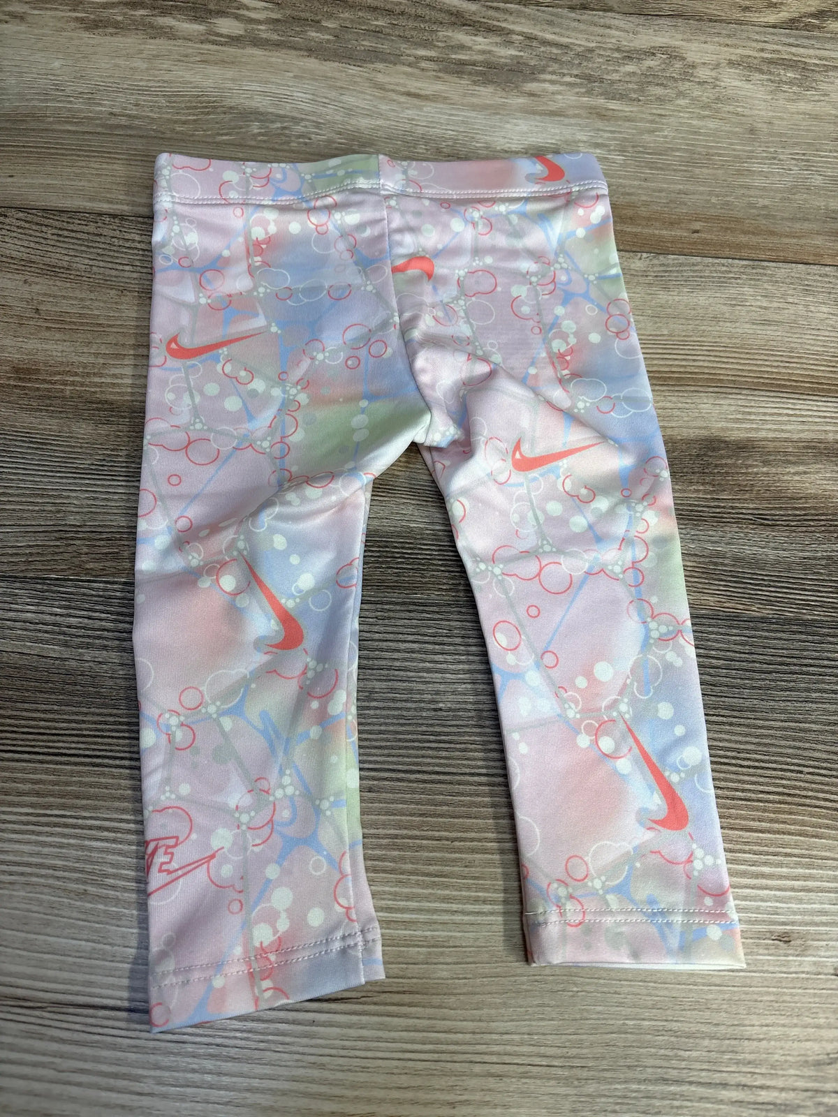 Flat lay of NEW Nike Leggings in pastel pink bubble print with orange Nike swoosh on wood plank floor