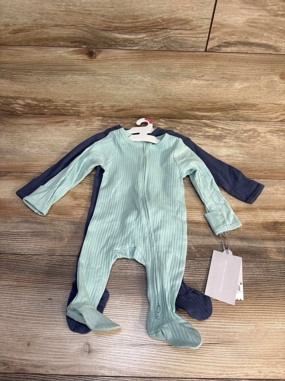Two ribbed baby footed pajamas in mint green and navy blue on wood floor