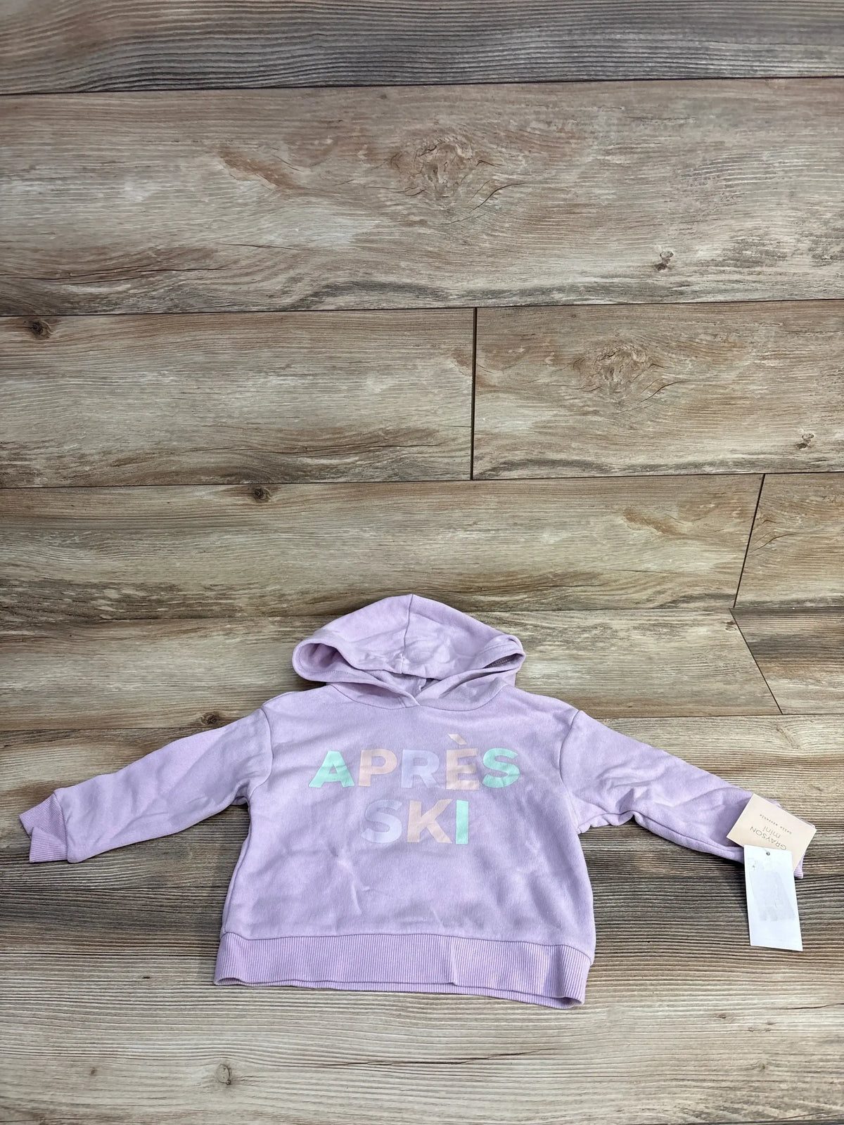 Light purple toddler hoodie with 'Après Ski' text, laid flat on wooden floor