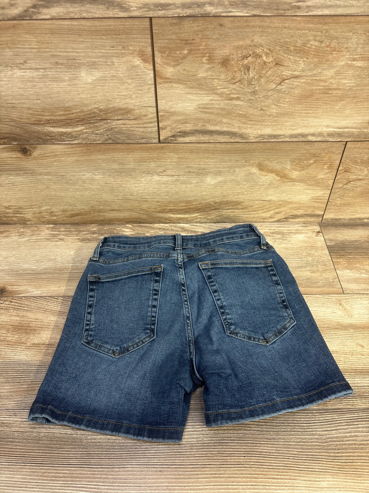 Back view of Gap maternity denim shorts in dark wash blue showcasing two functional back pockets on a wood floor