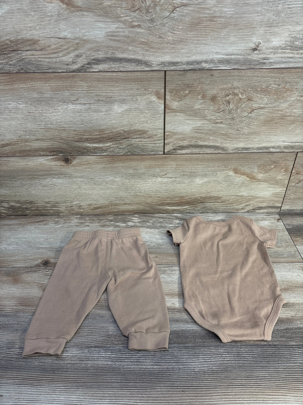 Flat lay of tan Nike 2-piece bodysuit and elastic-waist pants with cuffed ankles on wood plank background, size 6 months