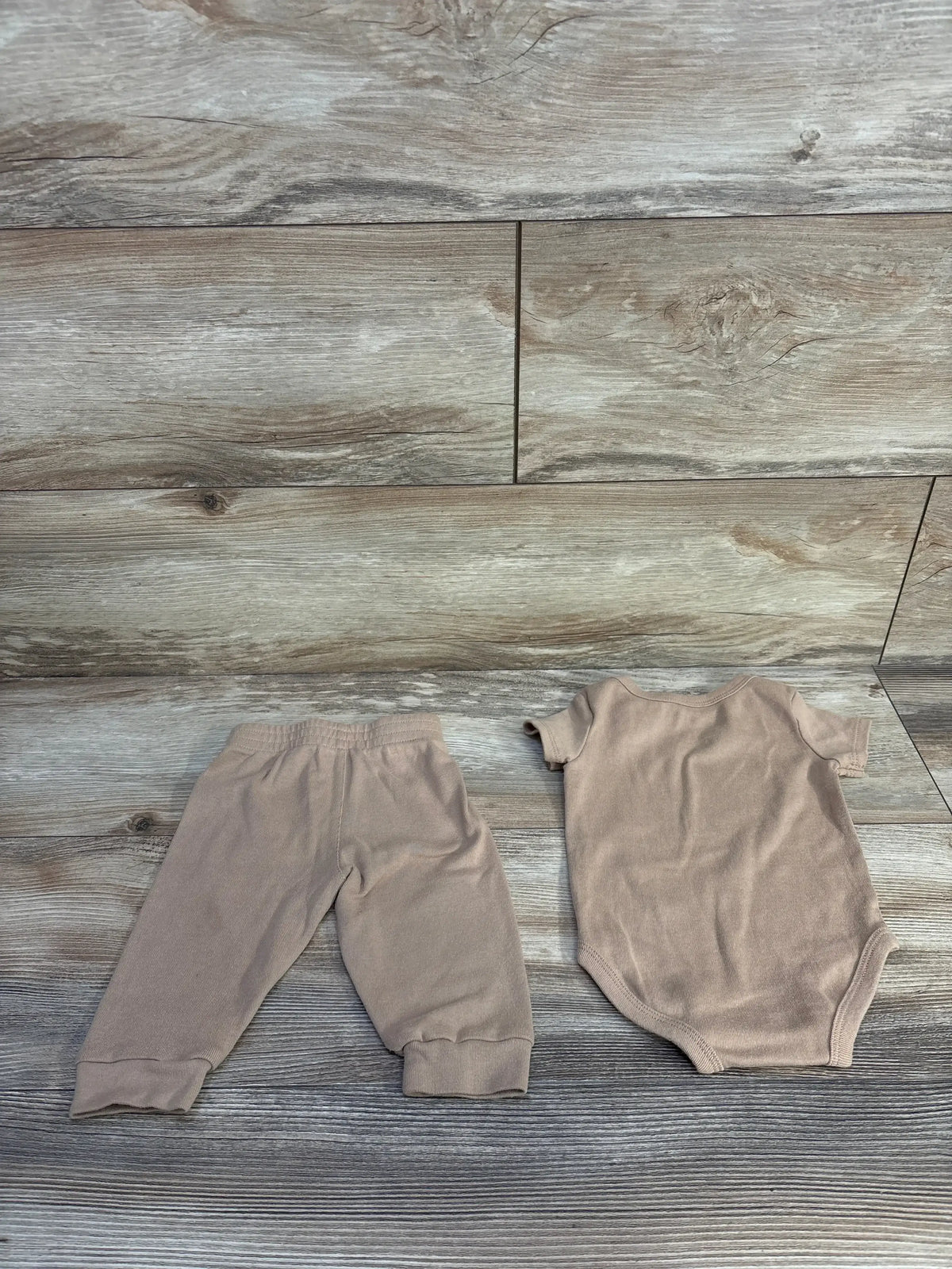 Flat lay of tan Nike 2-piece bodysuit and elastic-waist pants with cuffed ankles on wood plank background, size 6 months