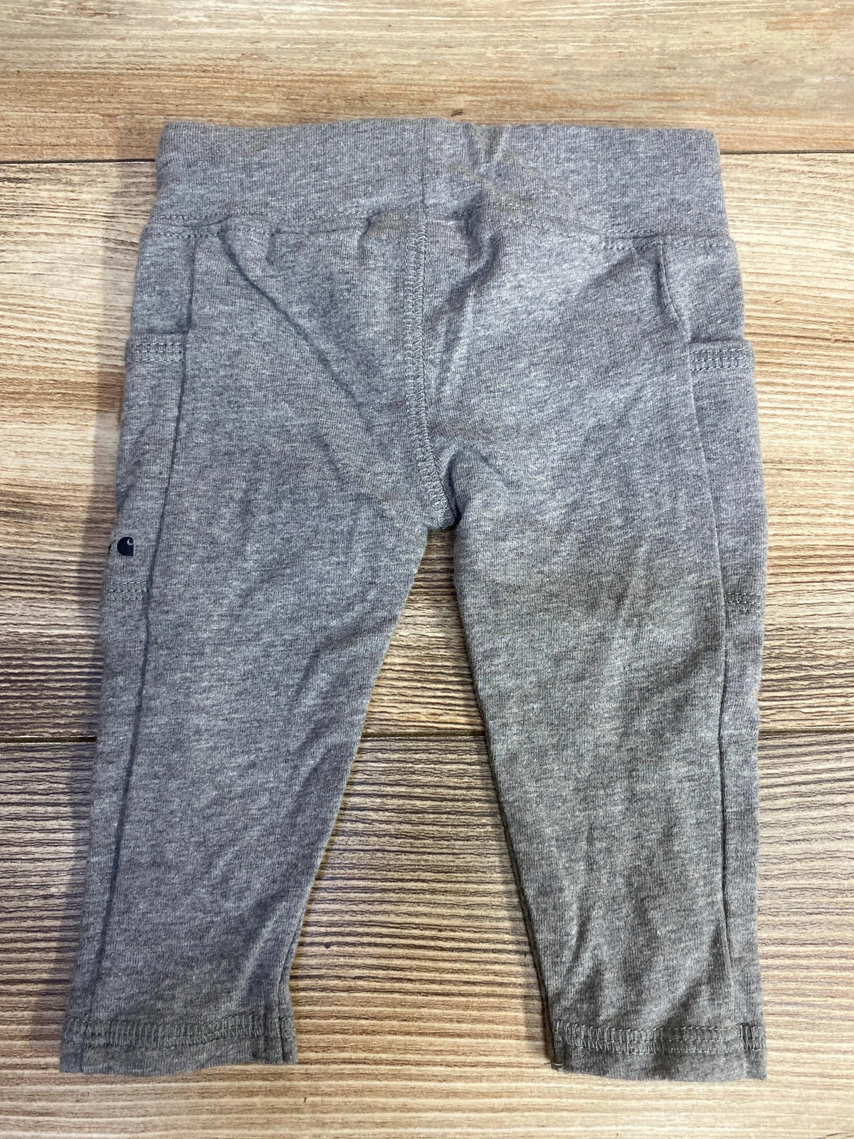 Front view of Carhartt gray leggings in size 3 months showcasing side pockets and logo on a wooden background