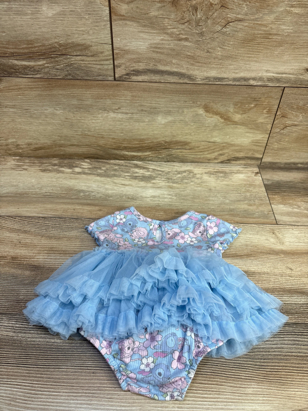 Front view of Disney Baby Stitch blue tutu bodysuit showcasing floral print and layered tulle on wood floor