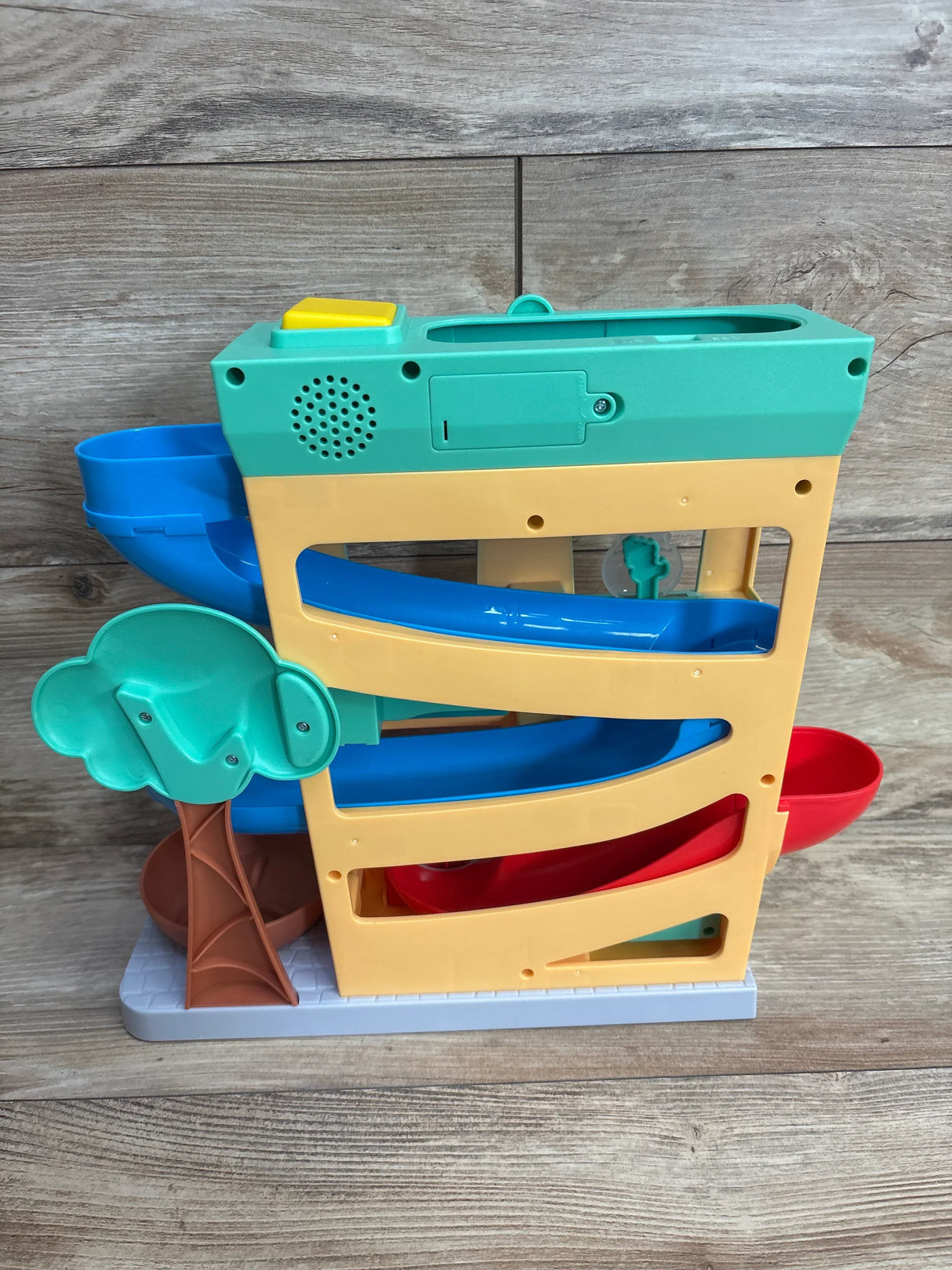 Colorful plastic toddler ramp toy with blue, red slides and a green tree on wood background