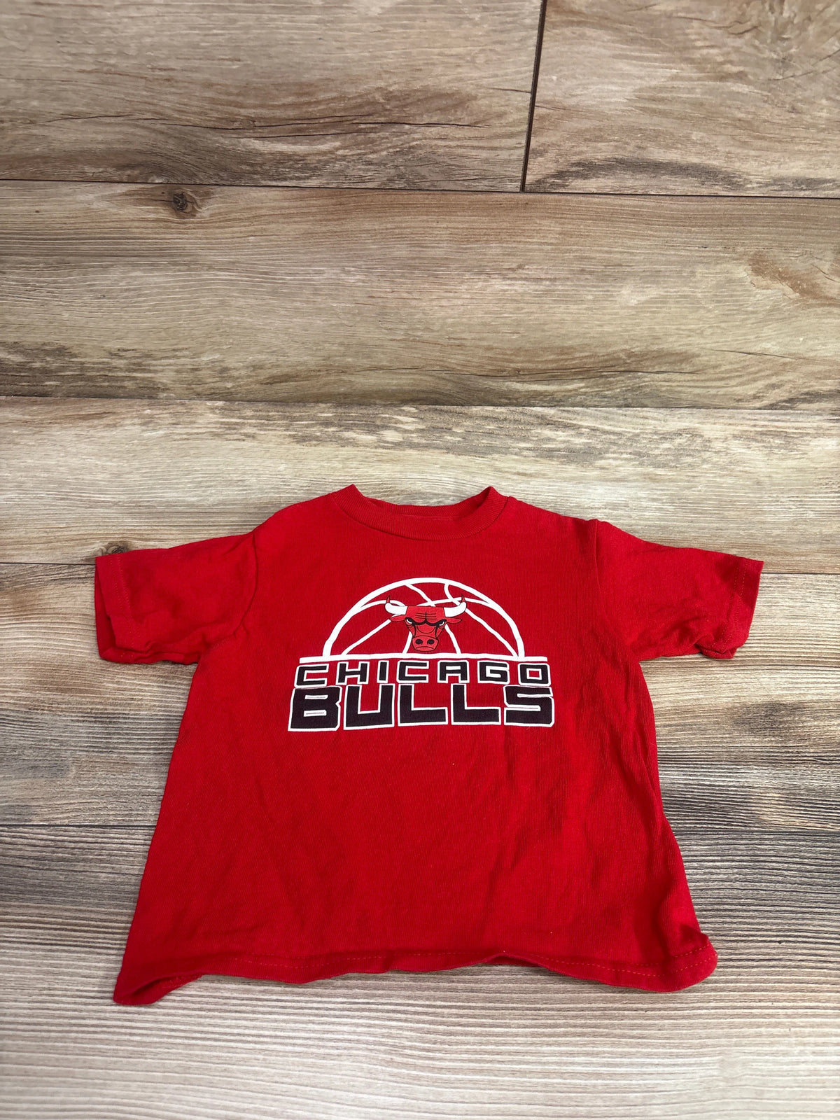 Front view of red Chicago Bulls toddler shirt showcasing bull logo and Chicago Bulls graphic on a wood floor
