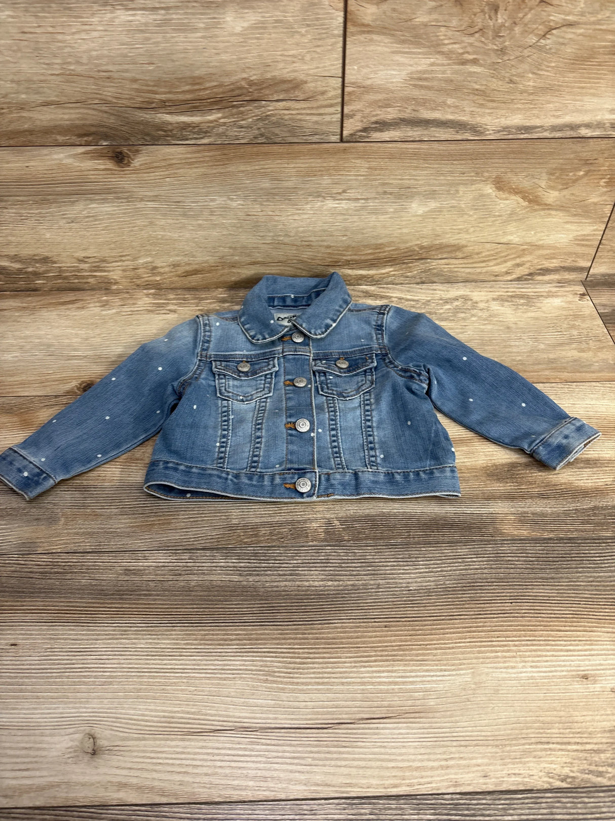 Light blue denim toddler jacket with front buttons and small white paint splatters on wooden floor