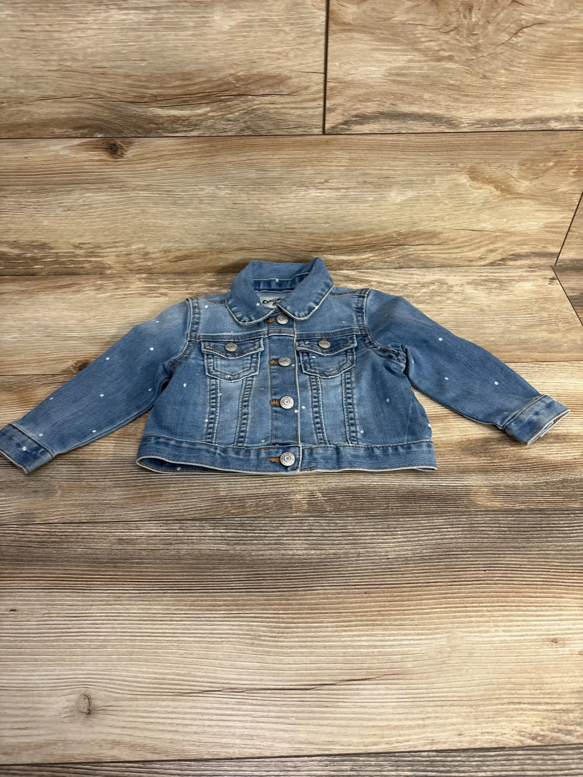 Light blue denim toddler jacket with front buttons and small white paint splatters on wooden floor