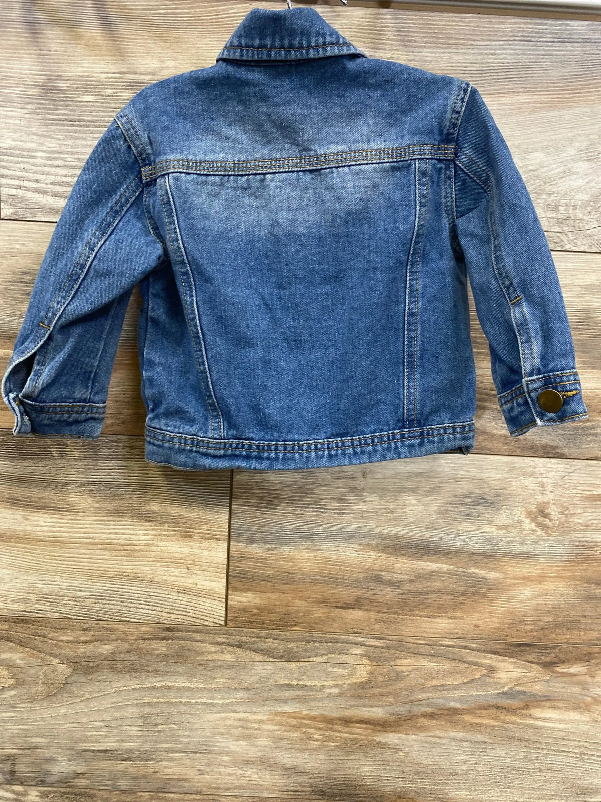 Kids blue denim jacket with long sleeves and button cuffs on wood background