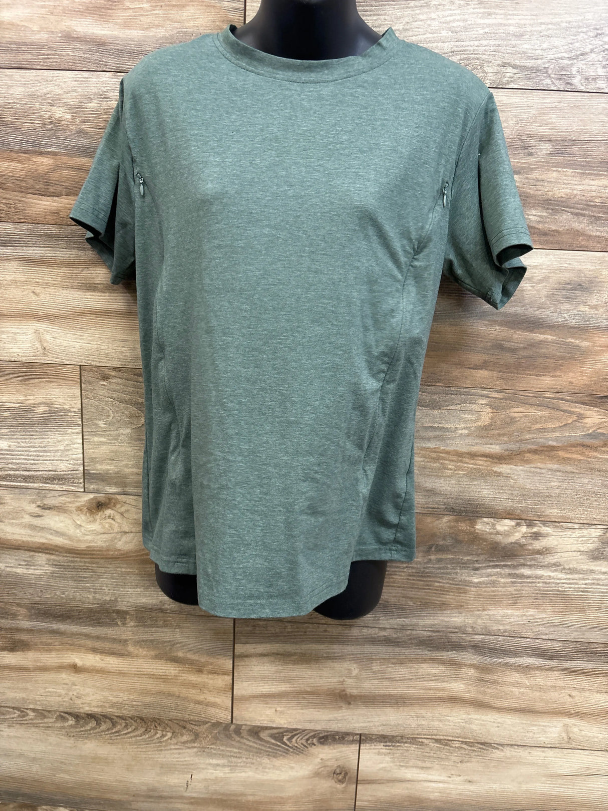 Front view of green zippered nursing T-shirt showing side nursing zippers on a black torso mannequin against a wood plank background