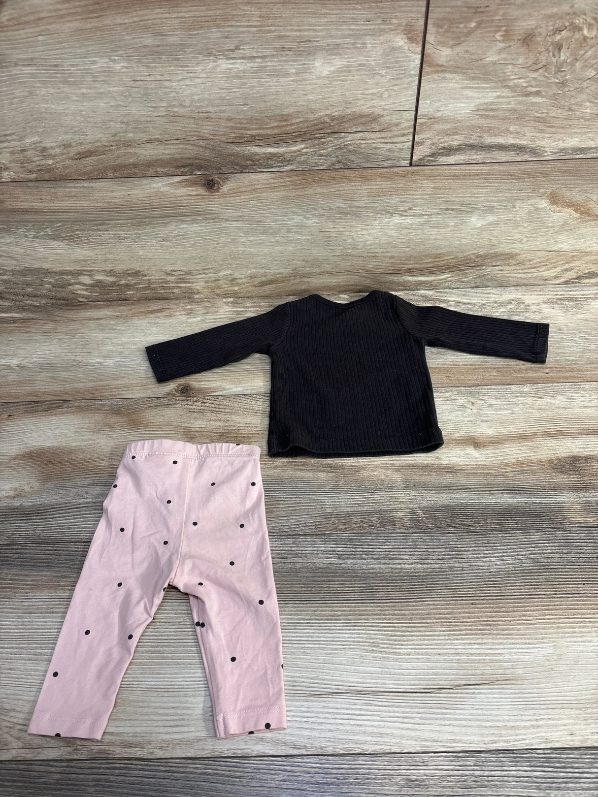 Children's outfit with black long-sleeve ribbed top and pink leggings with black polka dots on wooden floor