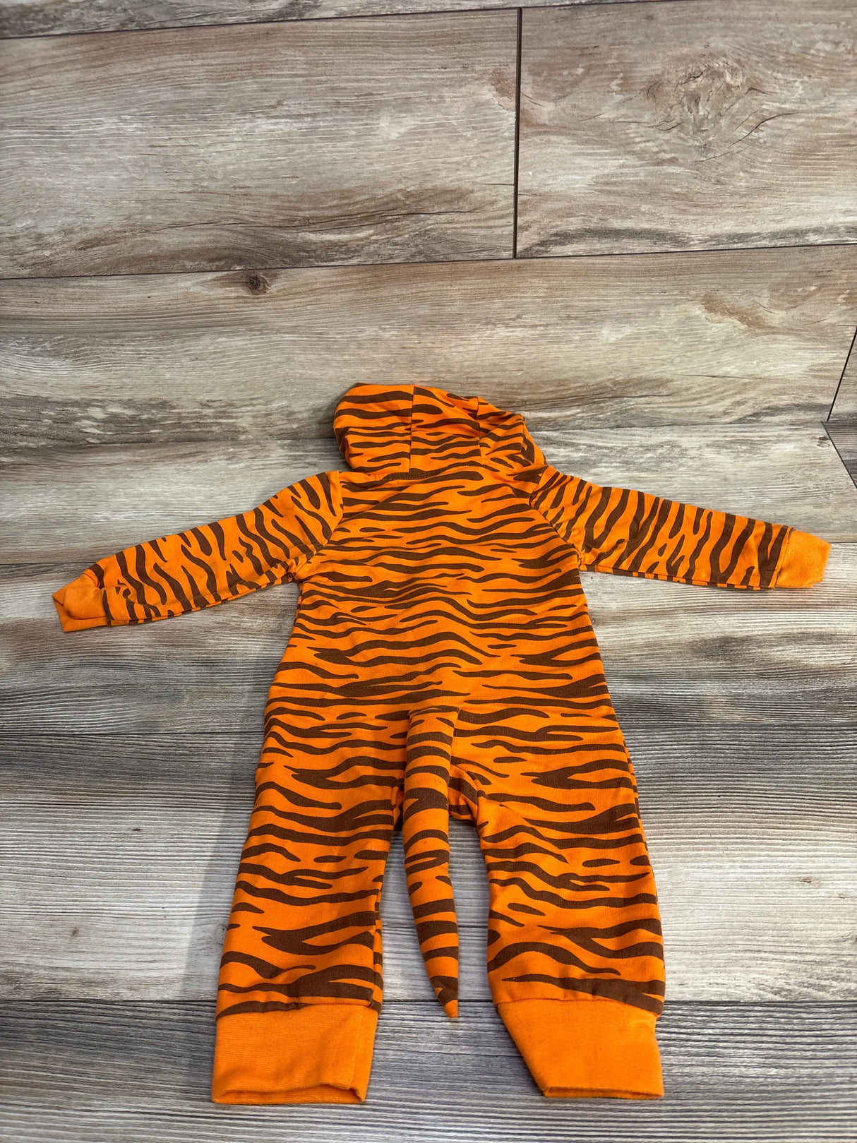 Orange and brown tiger stripe baby onesie with hood and tail, laid flat on wood floor
