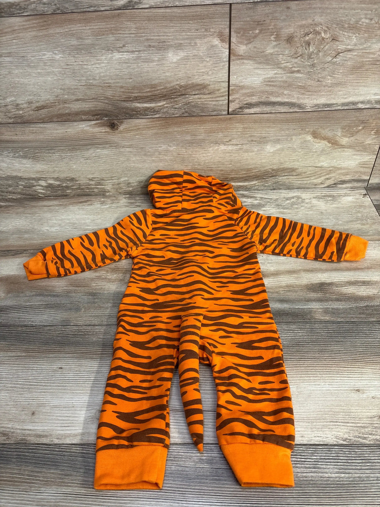 Orange and brown tiger stripe baby onesie with hood and tail, laid flat on wood floor