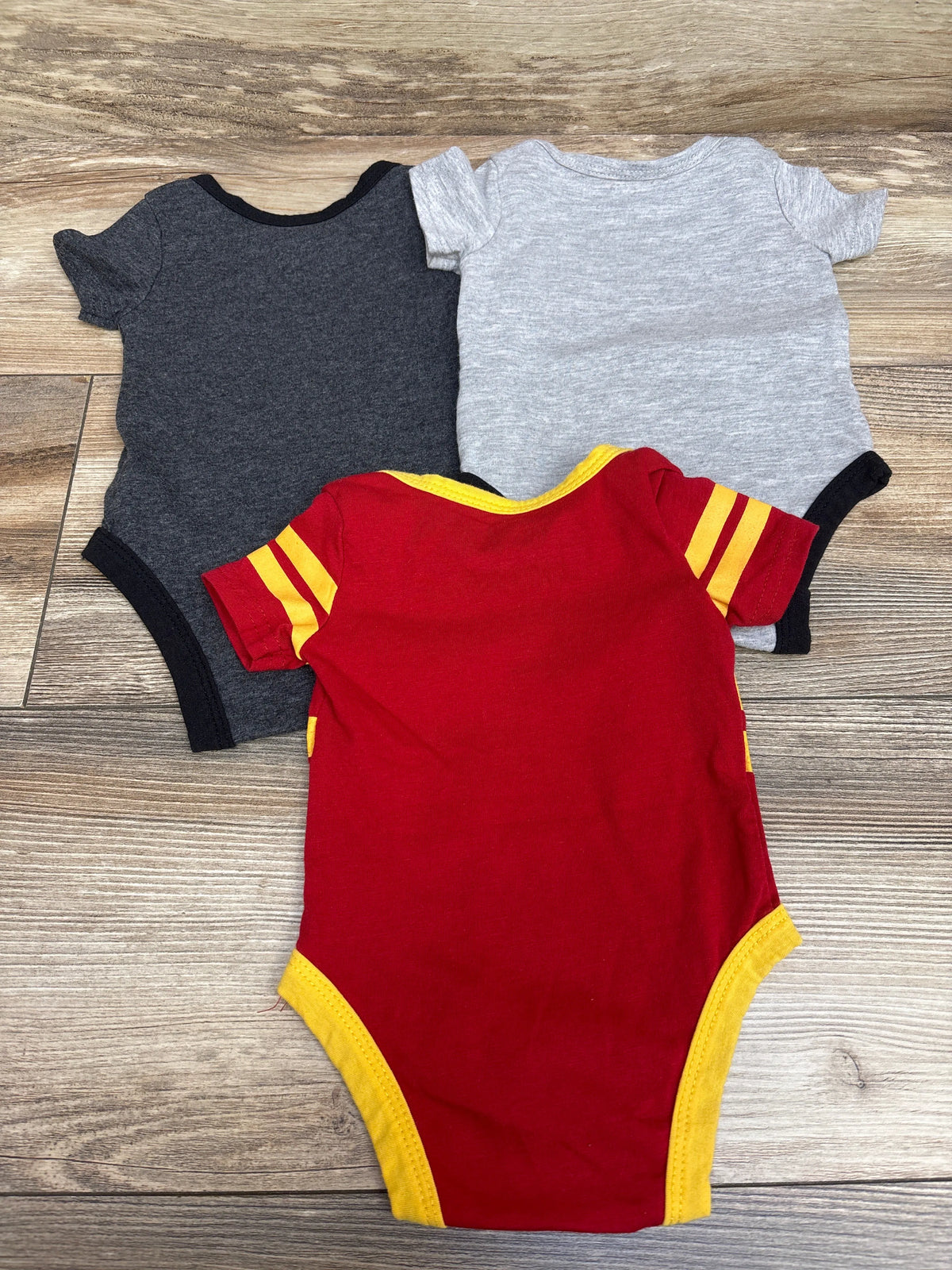 Top view of Wizarding World Harry Potter bodysuits in dark gray, light gray, and red with yellow trim on a wood floor