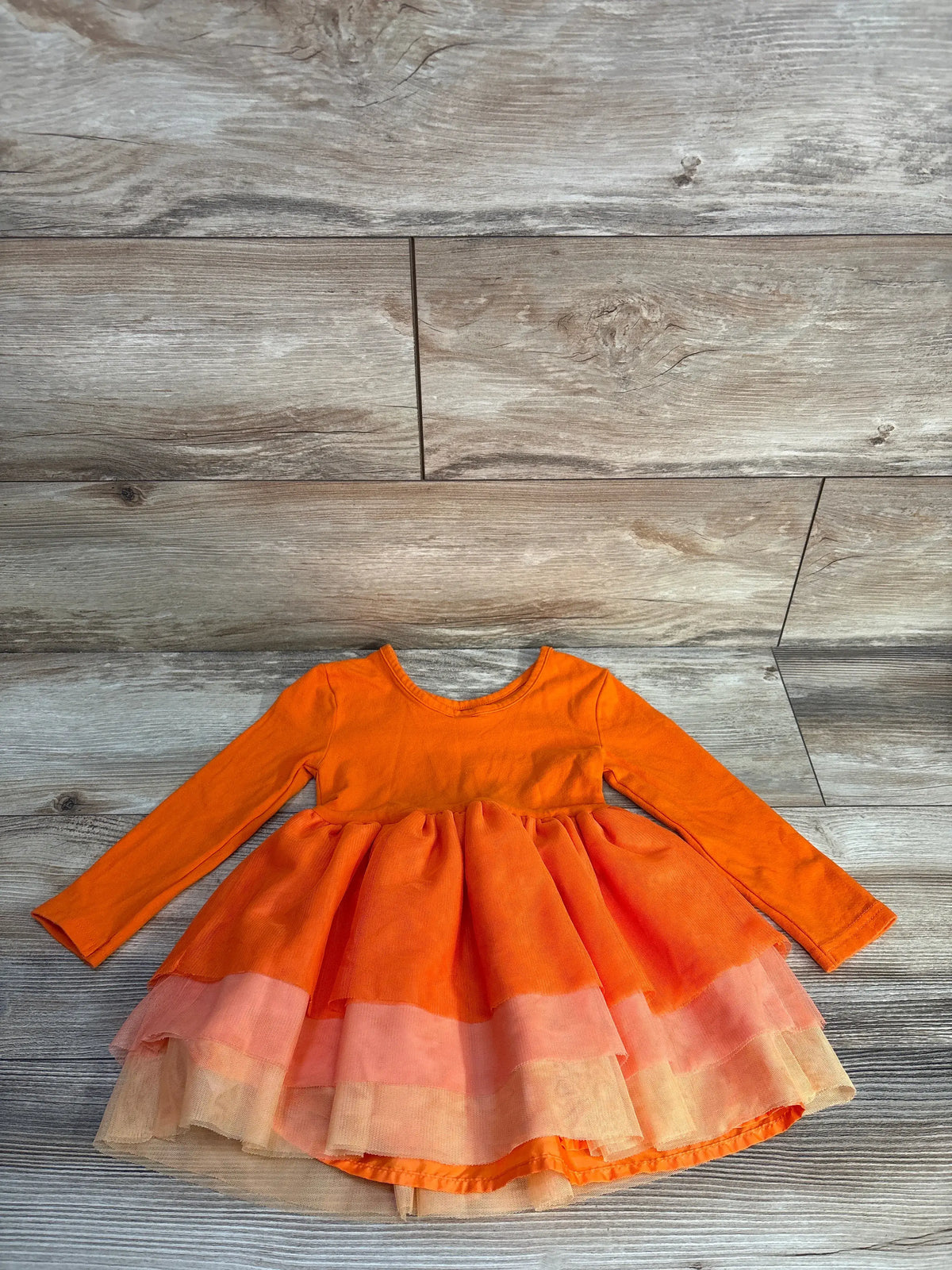 Front view of Old Navy fit and flare tutu dress showcasing pumpkin orange long sleeves, ruffled waist, and layered skirt on a wood-grain floor