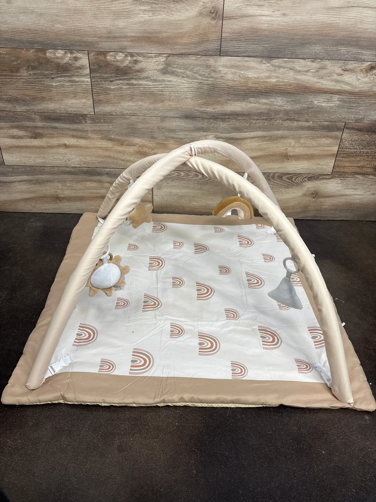 Neutral baby play gym mat with soft arches and hanging toys, rainbow print, on wood floor