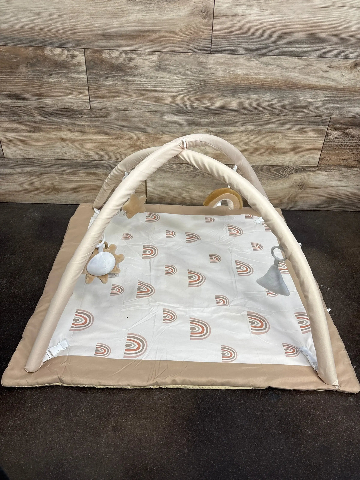 Neutral baby play gym mat with soft arches and hanging toys, rainbow print, on wood floor