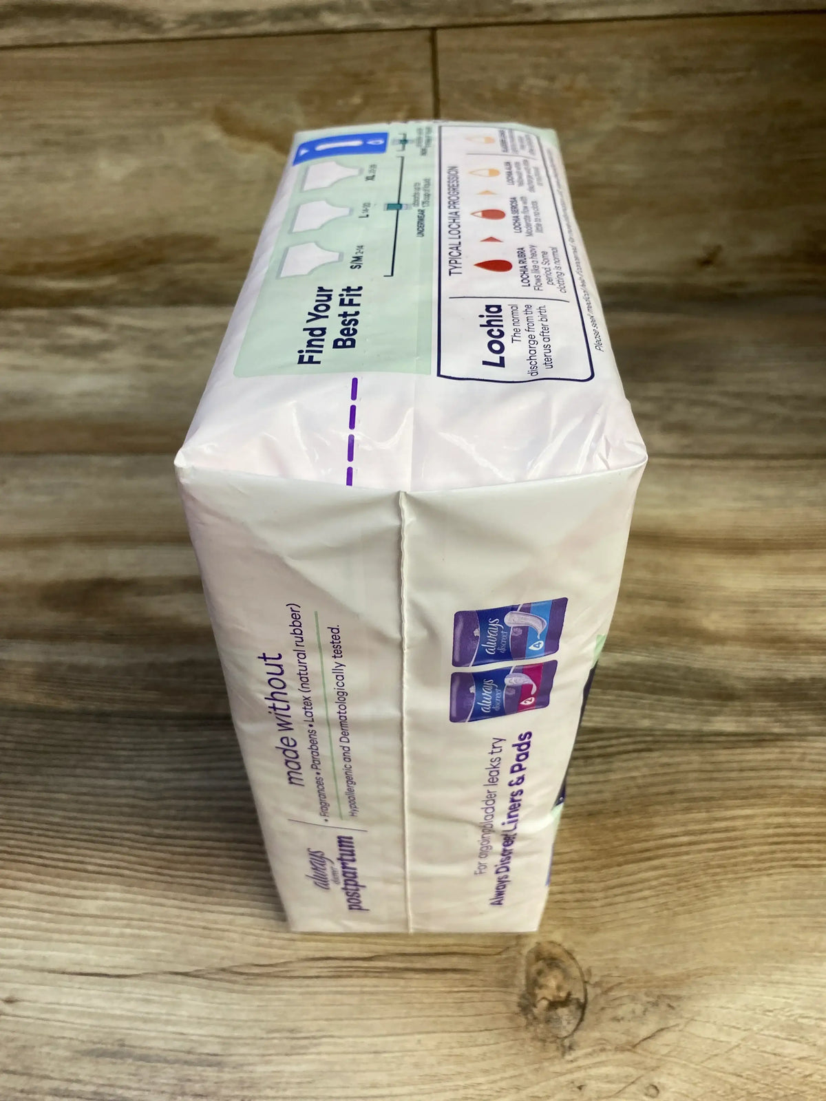 Side view of NEW Always Discreet Postpartum pads package showing Find Your Best Fit and Lochia progression info graphics on wood plank floor