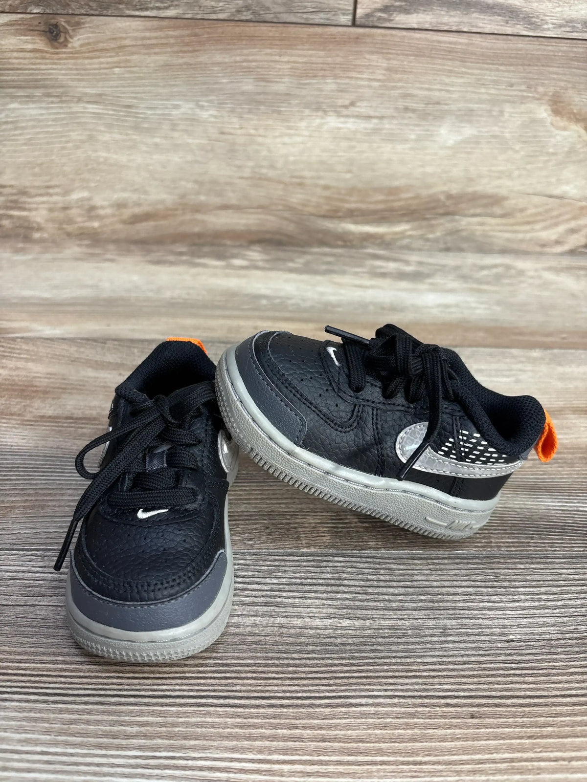 Pair of black and gray toddler Nike sneakers with orange heel tabs on wood background