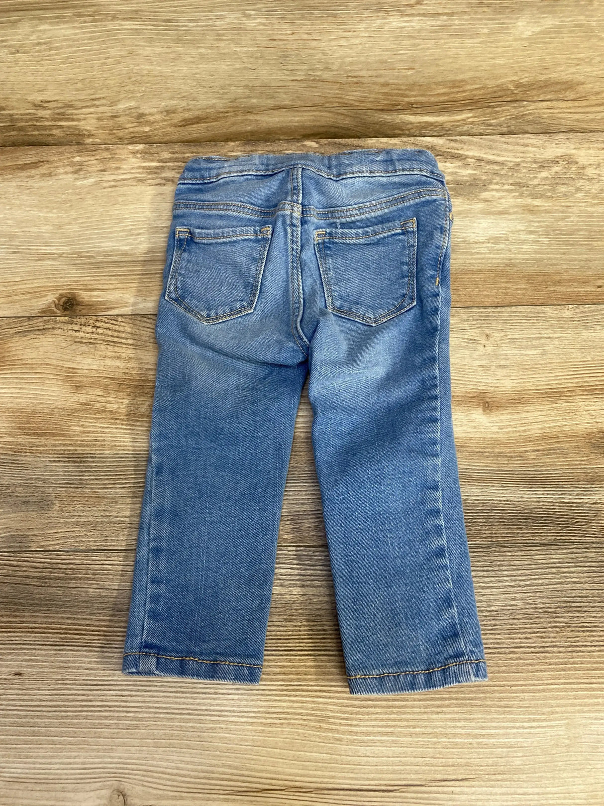 Back view of Old Navy toddler skinny jeans showcasing elastic waistband, two back pockets and slim legs on wooden surface, size 18-24 months