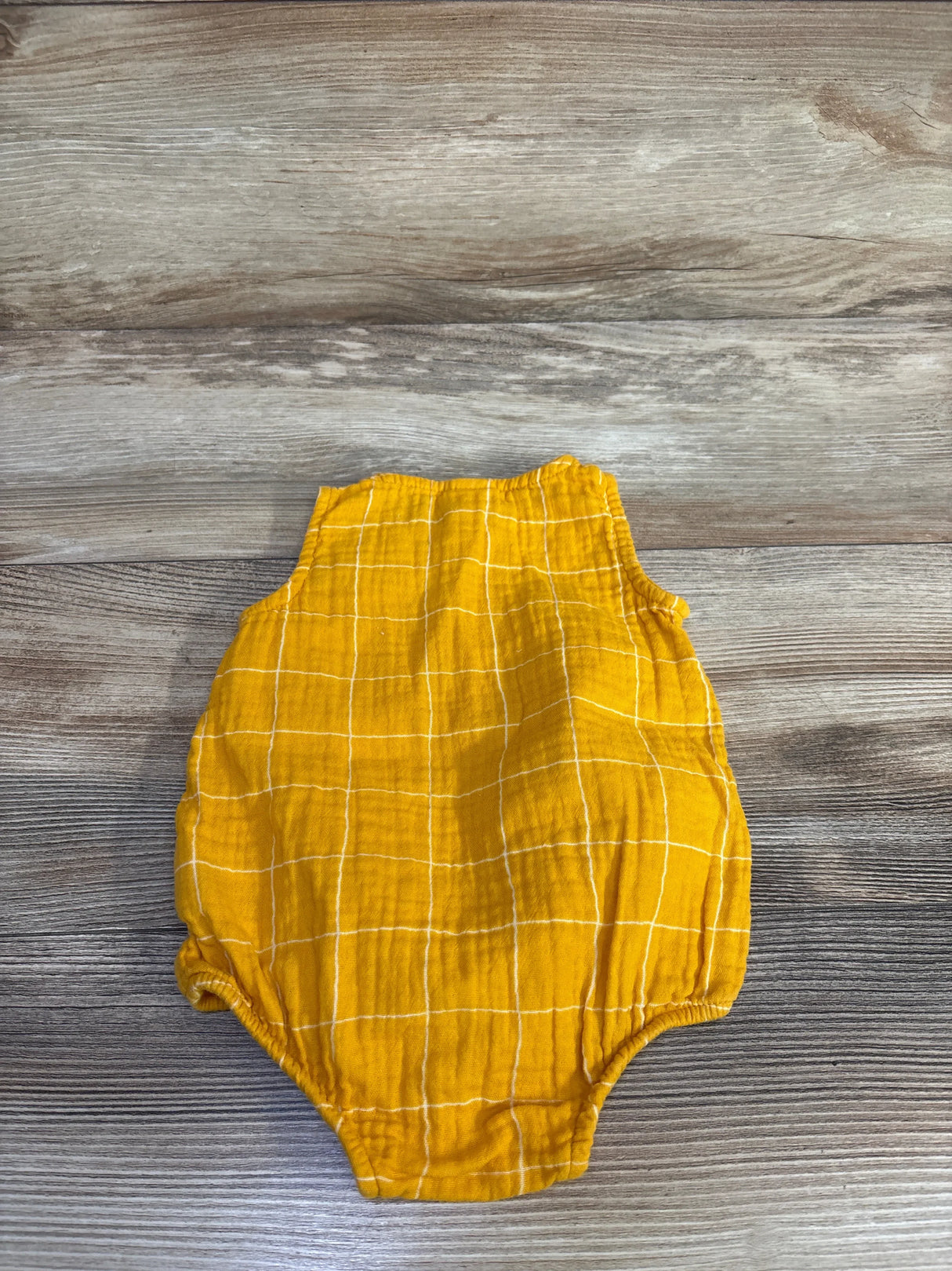 Top-down of yellow checkered tank bubble romper showing sleeveless top and elasticized leg openings on wood background
