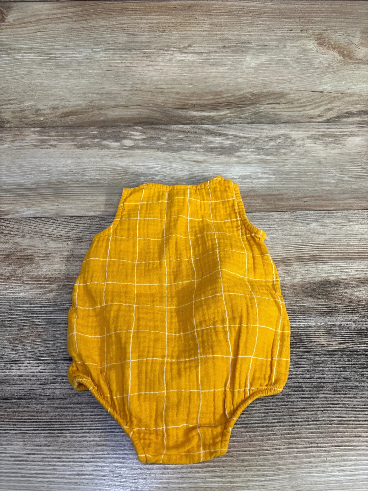 Top-down of yellow checkered tank bubble romper showing sleeveless top and elasticized leg openings on wood background