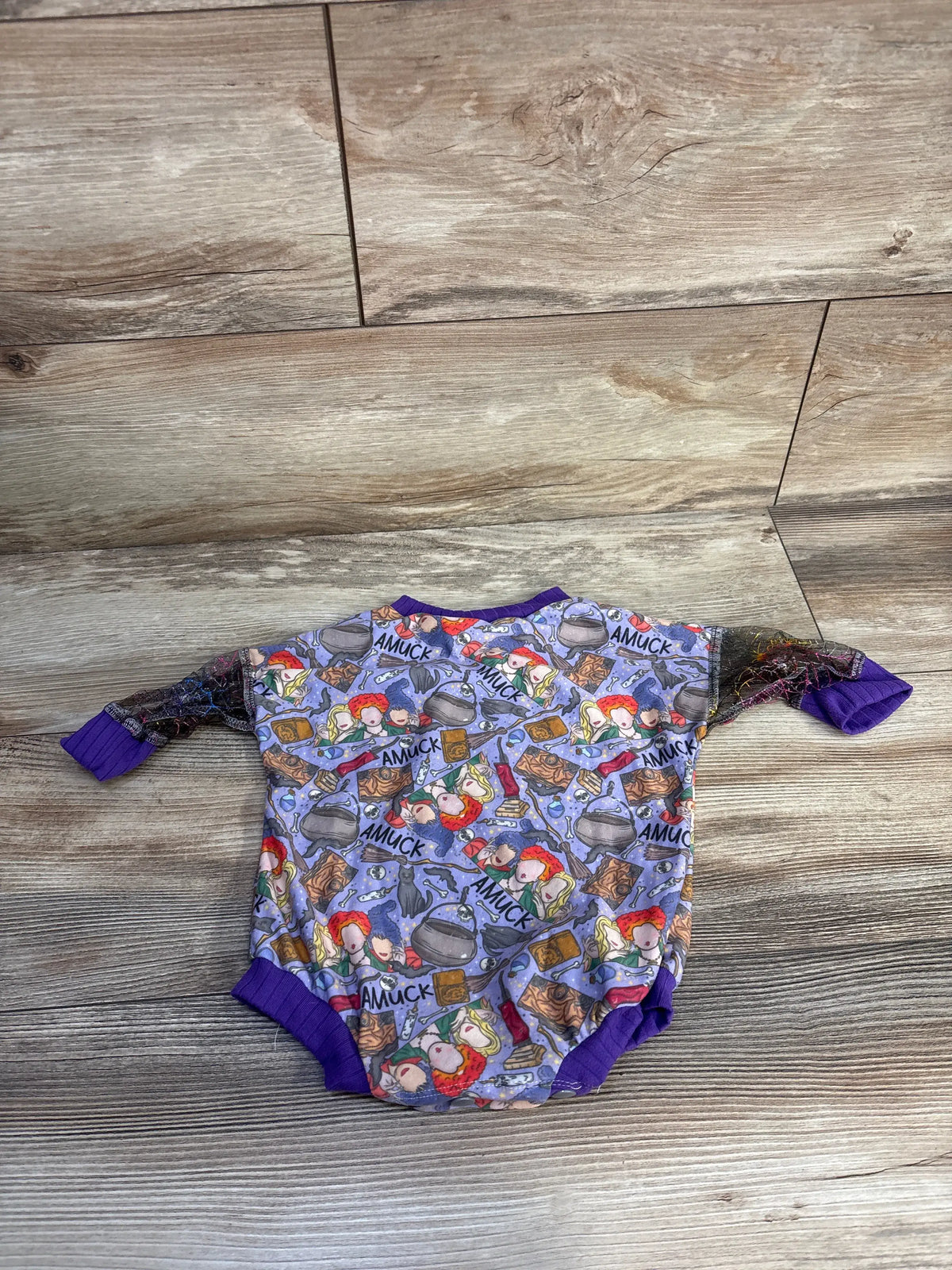 Front view of Ken & Co Hocus Pocus bubble romper in purple showcasing character and AMUCK print on a wood-grain floor