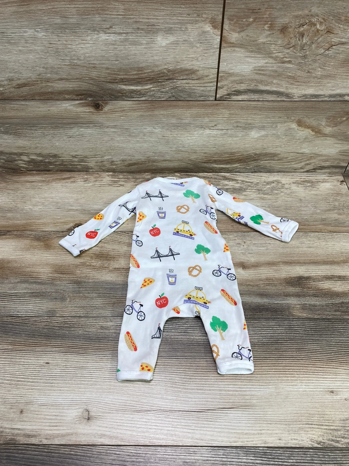 Flat lay of Estalla organic New York romper showing white long sleeve cotton with NYC themed print on wood background