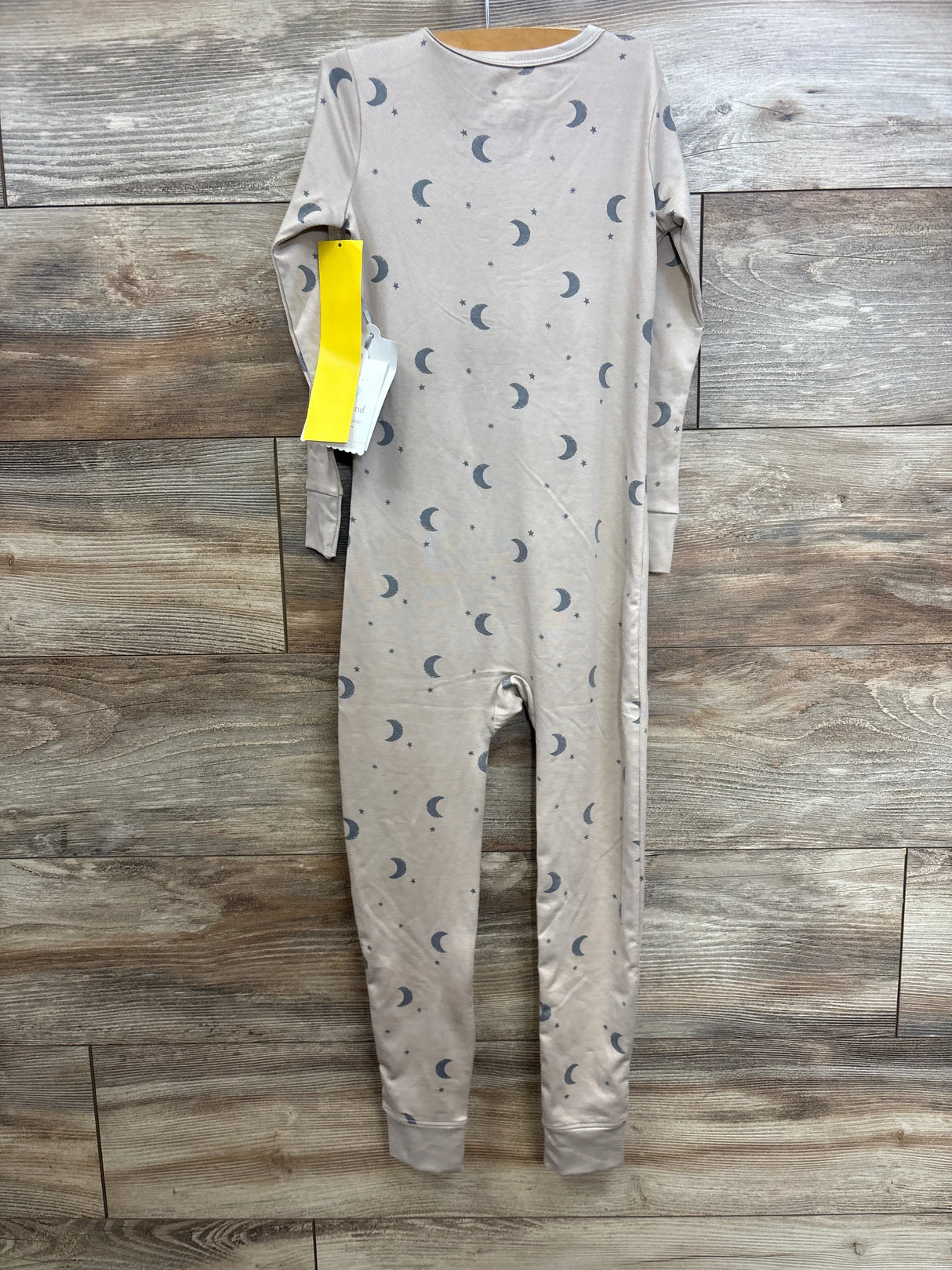 Front view of tan moon-print toddler sleeper (size 5T) with cuffed ankles, hanging on wooden hanger against wood-plank wall