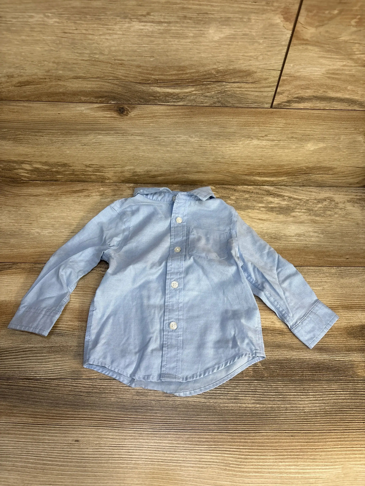Light blue long sleeve button-up baby shirt on wood background