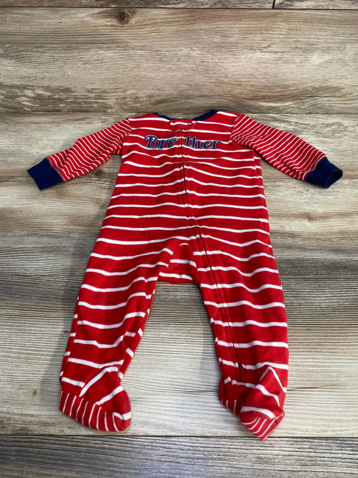 Flat lay of Carter’s red and white striped footed sleeper showcasing embroidered Brother text on chest, navy cuffs, and front zipper on wood background