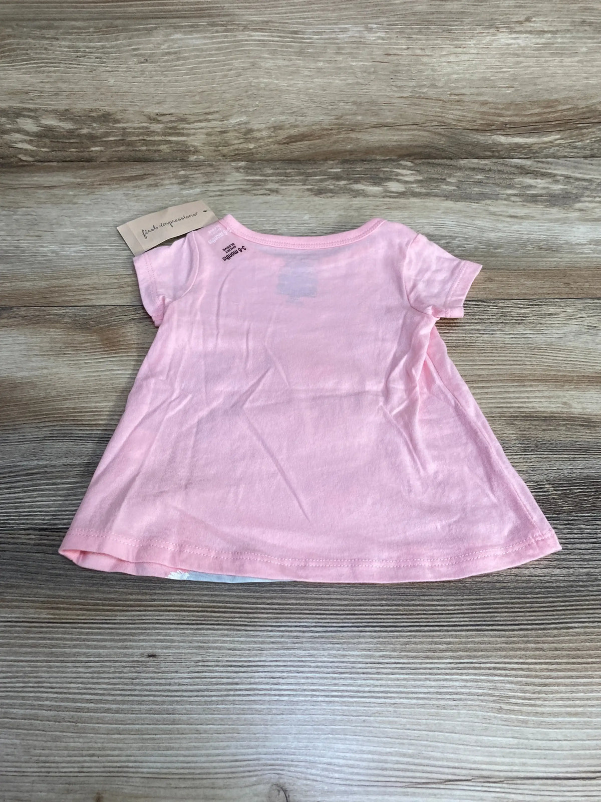Flat lay of pink First Impressions baby shirt 3-6 months showing short sleeves and A-line swing silhouette on wood background