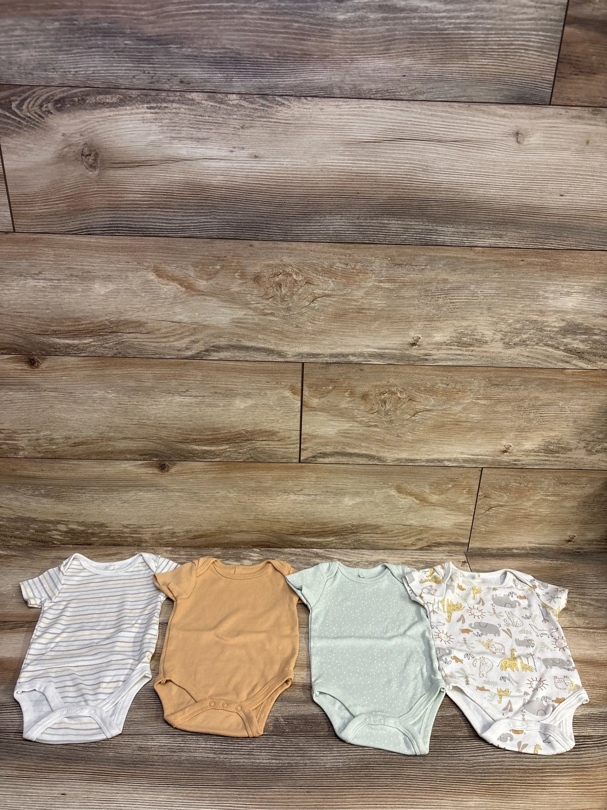 Top view of DreamGro 4pk bodysuits for 3 to 6 months showcasing four assorted colors and patterns on a wood floor