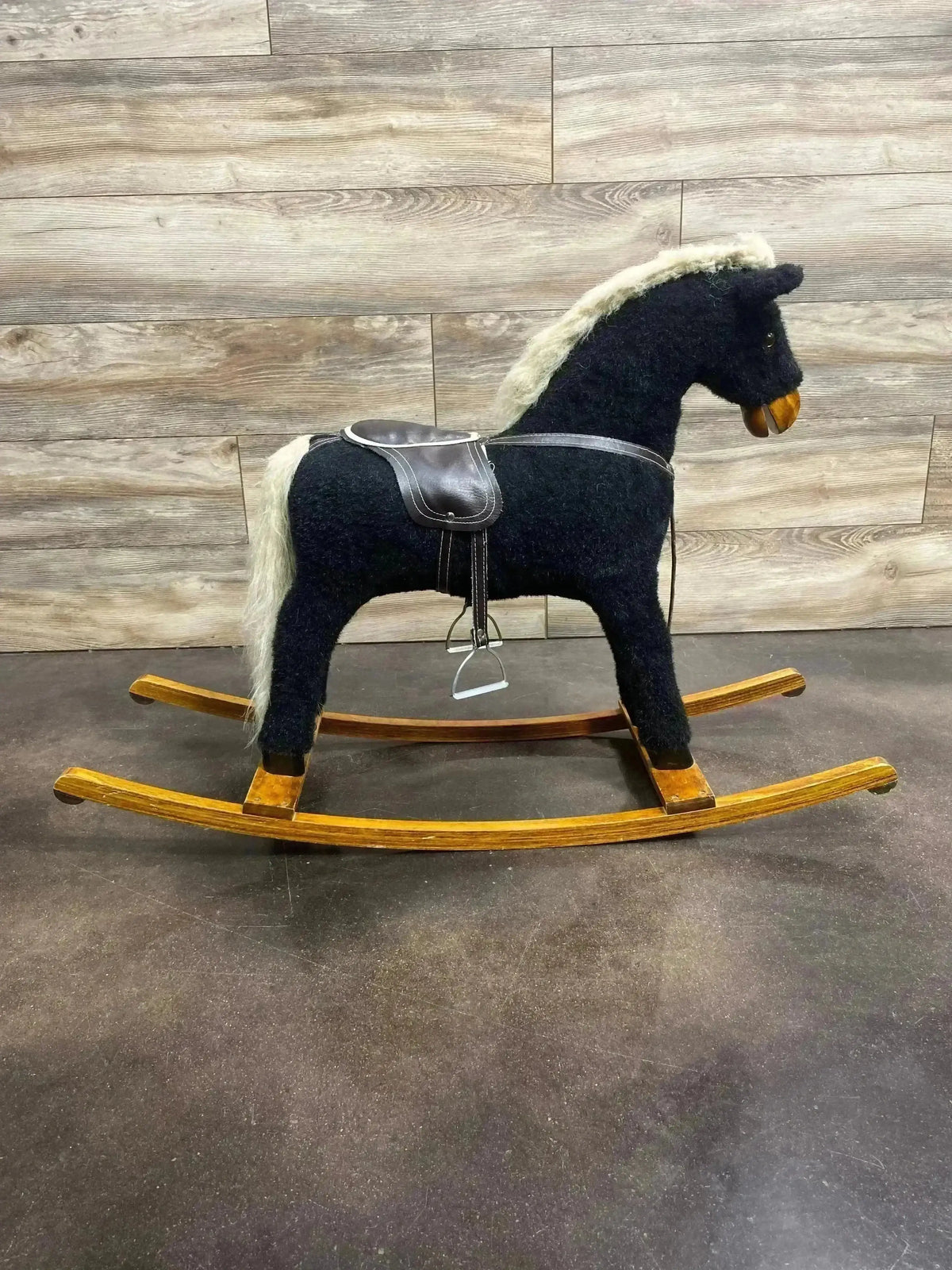 Side view of vintage Black Beauty rocking horse with black plush body, cream mane and tail, leather saddle on wooden rockers