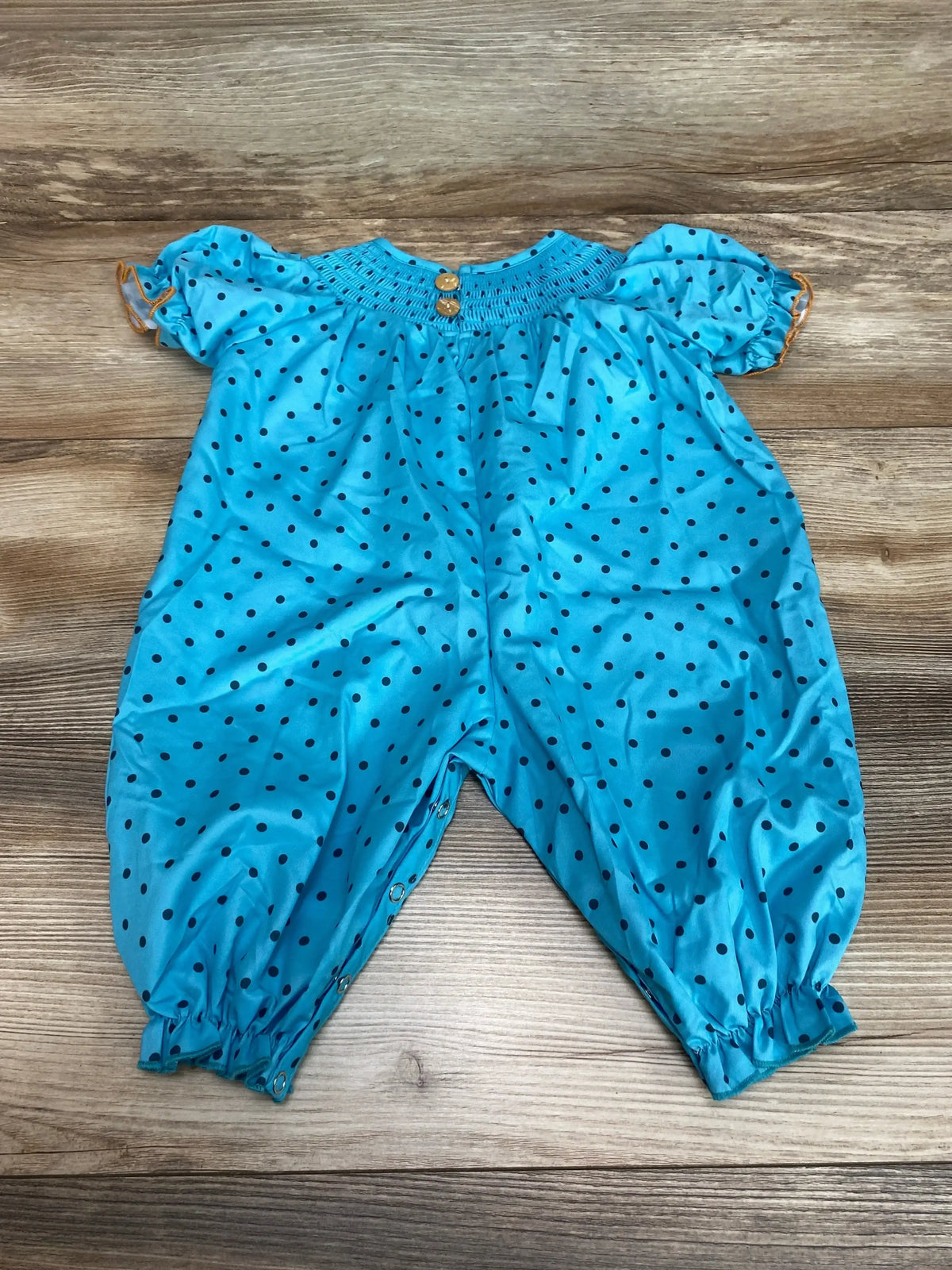 Front view of blue polka dotted smocked pumpkin romper with cinched sleeves and ankles on a wood surface