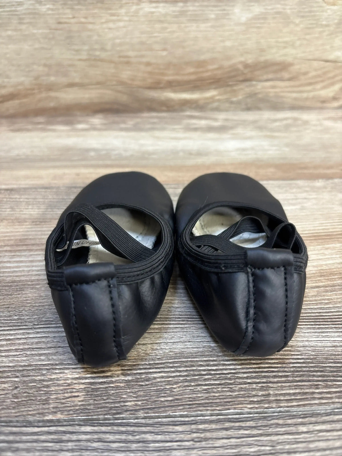 Pair of black leather children's ballet shoes with elastic straps on wood background