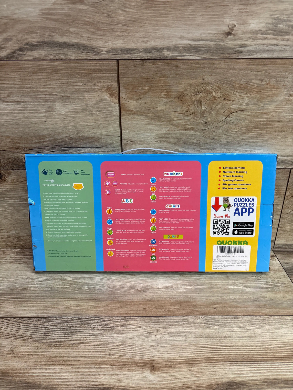 Back view of Quokka Interactive ABC Learning Poster showing ABC, numbers, colors, spelling, and game instructions on a wood surface