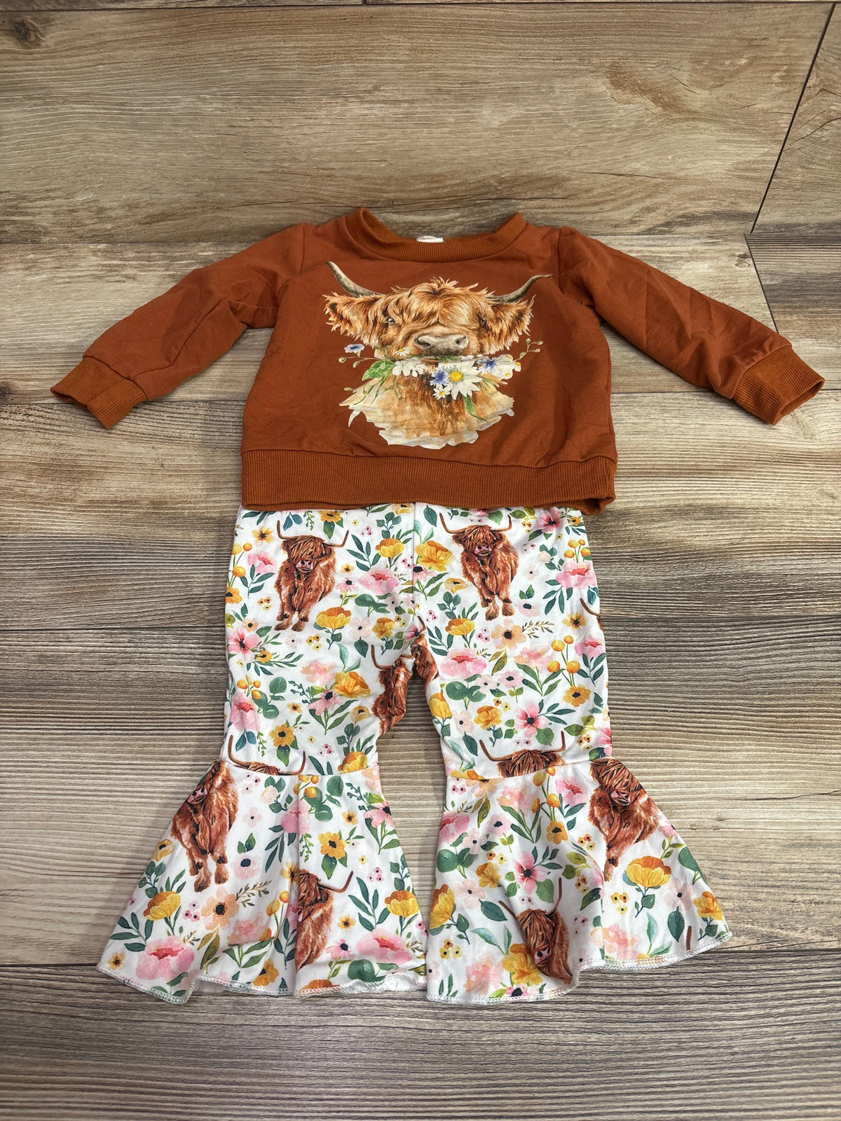 Top view of BULINGNA 2pc Highland Cow sweatshirt and flare pants set showcasing cow graphic and floral print on wood background