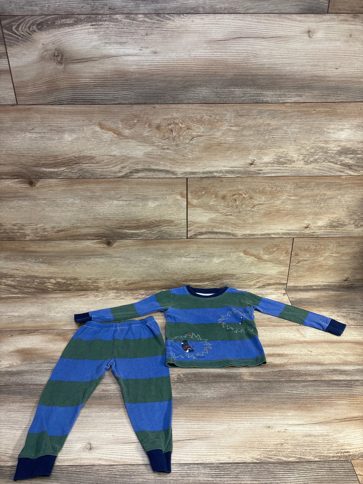 Flat-lay of 2-piece toddler pajama set, blue and green stripes, hedgehog patch on top, navy cuffs, elastic-waist pants