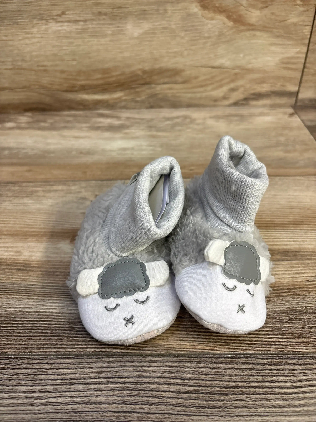 Soft baby booties with sheep face design in grey and white on wooden surface