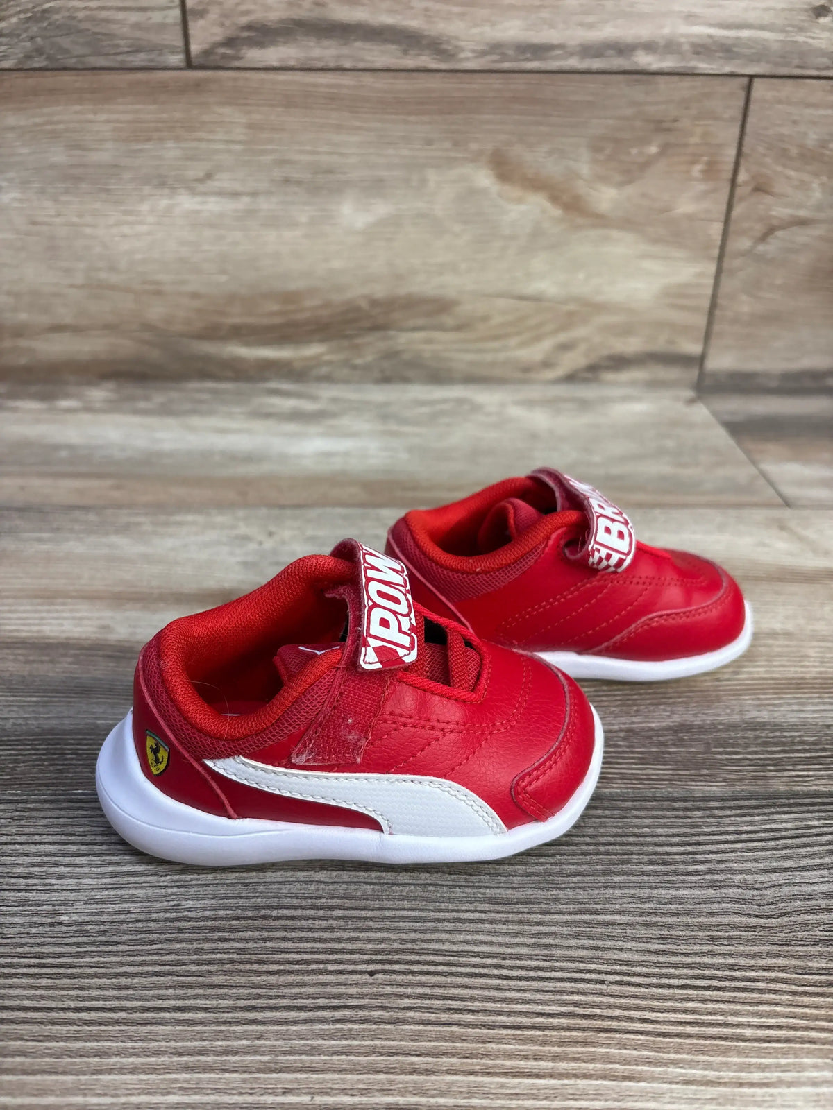 Front and side view of red Puma x Scuderia Ferrari Kart Cat III sneakers showcasing hook and loop closures on wood flooring