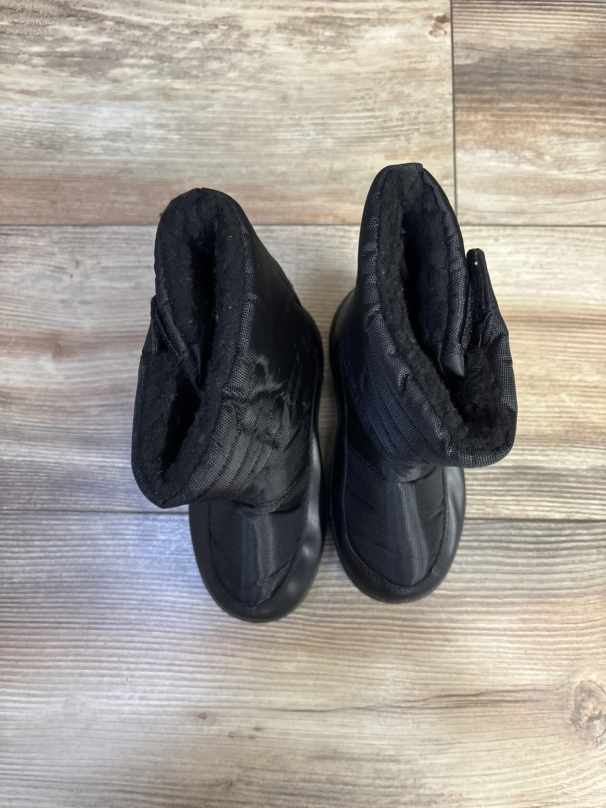 Top-down view of toddler black snow boots showcasing quilted nylon upper and fleece lining on light wood floor